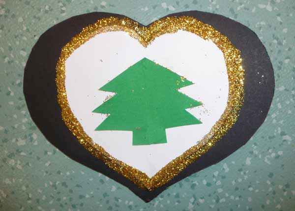 carte de Noël en forme de coeur avec un petit sapin en papier vert collé au centre et des paillettes